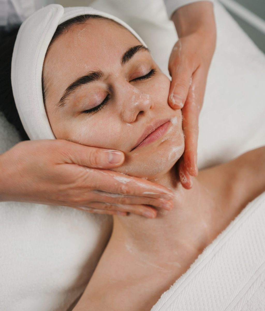 Beautician's hands applying foam cleanser for massaging client's face. Healthy skin care, exfoliation scrub soap with cleansing product. Skincare spa relax concept.